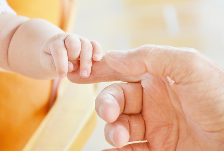 Babyhand hält den Finger einer älteren Hand